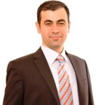 A man in a suit and tie standing confidently with a slight smile against a plain white background.
